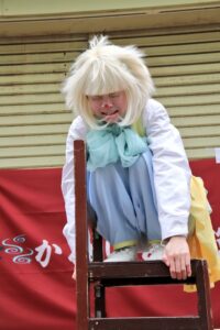 ピエロ(クラウン)のロイくんが椅子の上で泣きそうになっています。かめいど勝運大道芸2019で行われたアルジェントさーかすでのワンシーン